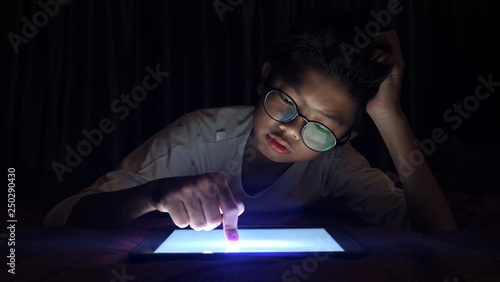 Asian boy pressing digital tablet at night with serious face.