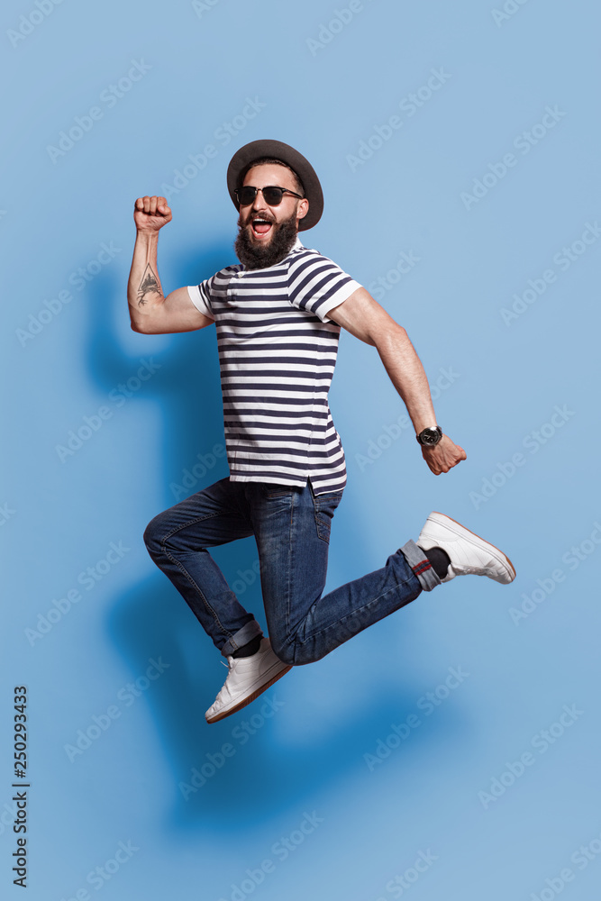 Trendy jumping hipster on blue backdrop  - obrazy, fototapety, plakaty 