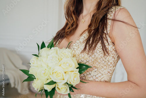 Crop photo of bride in beautiful golden dress with wedding bouquet of white roses in hands, close up
