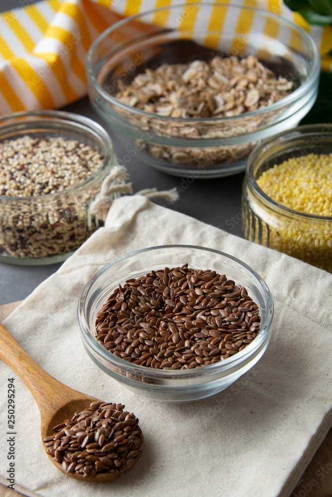 Brown flax seeds, closeup in glass bowl with variouse cereals on the background. Healthy food for breakfast, cereals. Food ingredient.