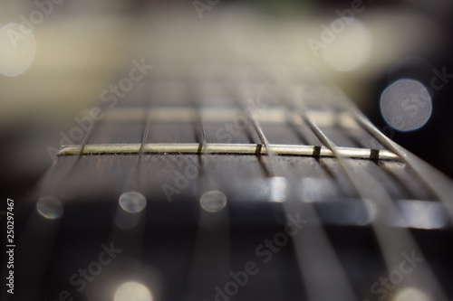 A photo of a guitar neck with strings and a wood texture - the material of a guitar neck. Selective focus on one guitar threshold. The strings rattle.