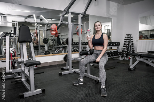 Woman in gym holding bottle of water and having rest