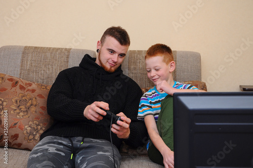 Happy father and son play video games at home, excited smile to hold the controller of the console in their hands, sitting on the couch, tv on the footpath