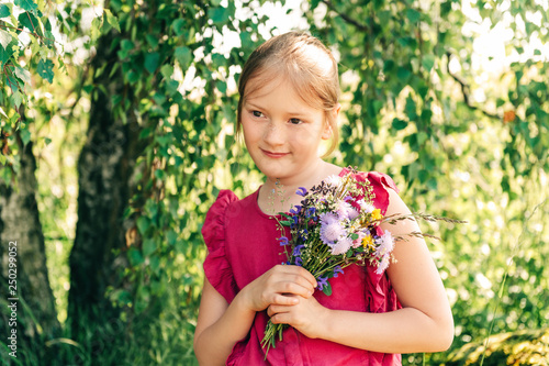 Summer portrait of cute little girl holding small bouquet of wild flowers
