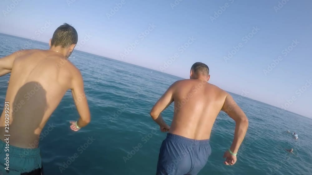 Two sportive men jumping feet first in the Red Sea from a platform in summer Two sportive men jumping feet first in the Red Sea from a platform in summer