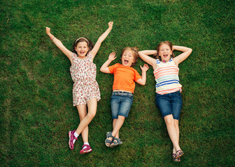 Happy children having fun outdoors. Kids playing in summer park. Little boy and two girls lying on green fresh grass