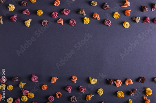 Multicolored pasta with the addition of natural vegetable dye. Scattered on a black background, copy space. Top view, pattern.