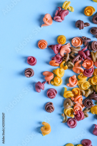 Multicolored pasta with the addition of natural vegetable dye. Scattered on a blue background. Top view, pattern.