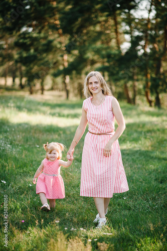 The mother runs with a daughter and holds her hand on nature on summer day, vacation. Mom and girl walking and playing in the park at the sunset time. Concept of friendly family. Close Up.