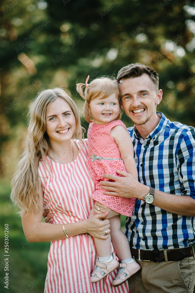 Portrait of a happy young family spending time together on nature, on vacation, outdoors. Mom, dad and daughter stand in the green grass. The concept of family holiday. Portrait of a happy young family spending time together on nature, on vacation, outdoors. Mom, dad and daughter stand in the green grass. The concept of family holiday.