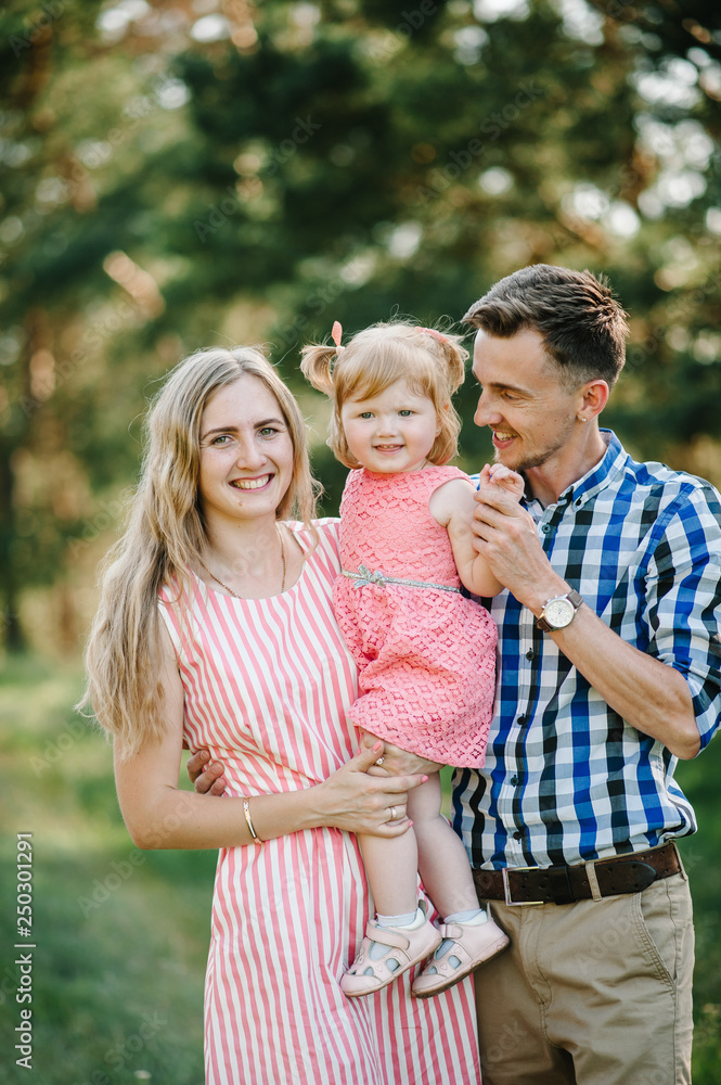 Portrait of a happy young family spending time together on nature, on vacation, outdoors. Mom, dad and daughter stand in the green grass. The concept of family holiday. Portrait of a happy young family spending time together on nature, on vacation, outdoors. Mom, dad and daughter stand in the green grass. The concept of family holiday.