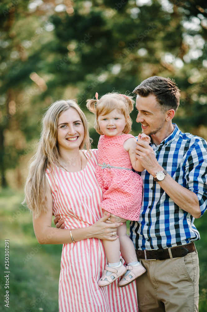 Portrait of a happy young family spending time together on nature, on vacation, outdoors. Mom, dad and daughter stand in the green grass. The concept of family holiday.