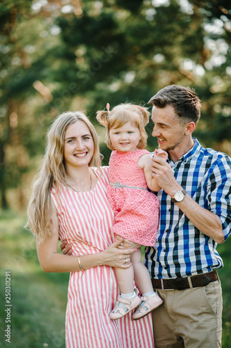 Portrait of a happy young family spending time together on nature, on vacation, outdoors. Mom, dad and daughter stand in the green grass. The concept of family holiday. © Serhii