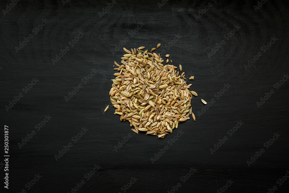Close-up image of fennel seeds on black wood background, view above