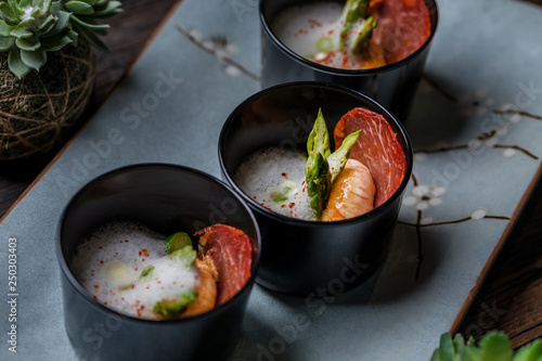 Lobster shrimp appetizer with parma ham, asparagus and white mousse sauce in black bowl on rustic wooden table 