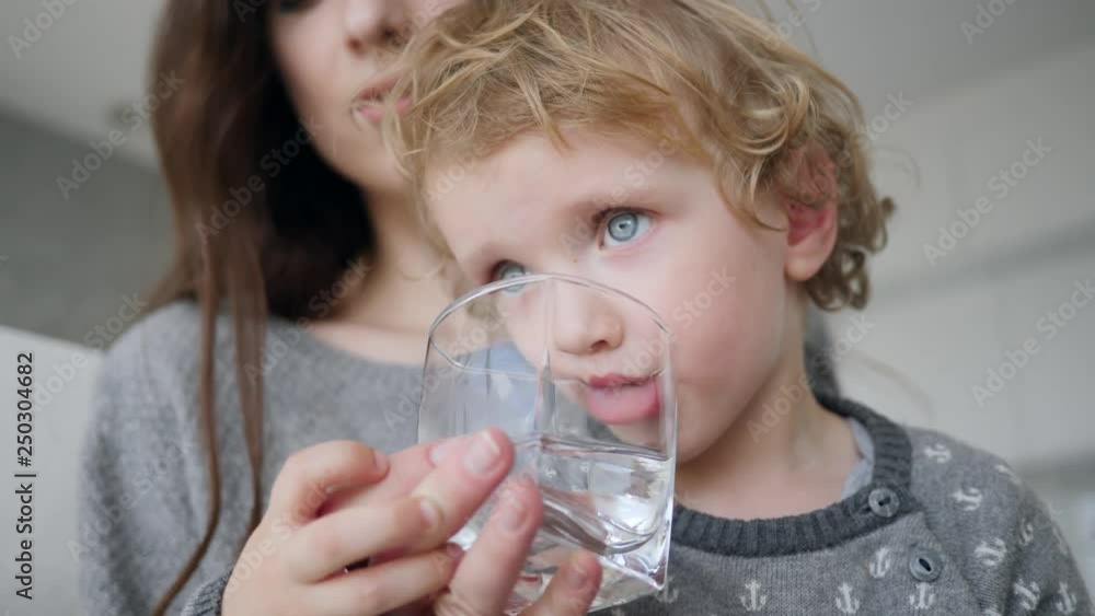 Cute little baby boy at home drinking clean fresh water from a glass cup closeup Cute little baby boy at home drinking clean fresh water from a glass cup closeup