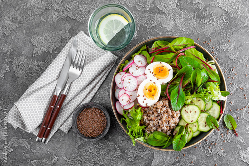 Buddha bowl dish with buckwheat porridge, boiled egg, fresh vegetable salad of radish, cucumber, lettuce and chard leaves. Healthy lunch menu. Top view