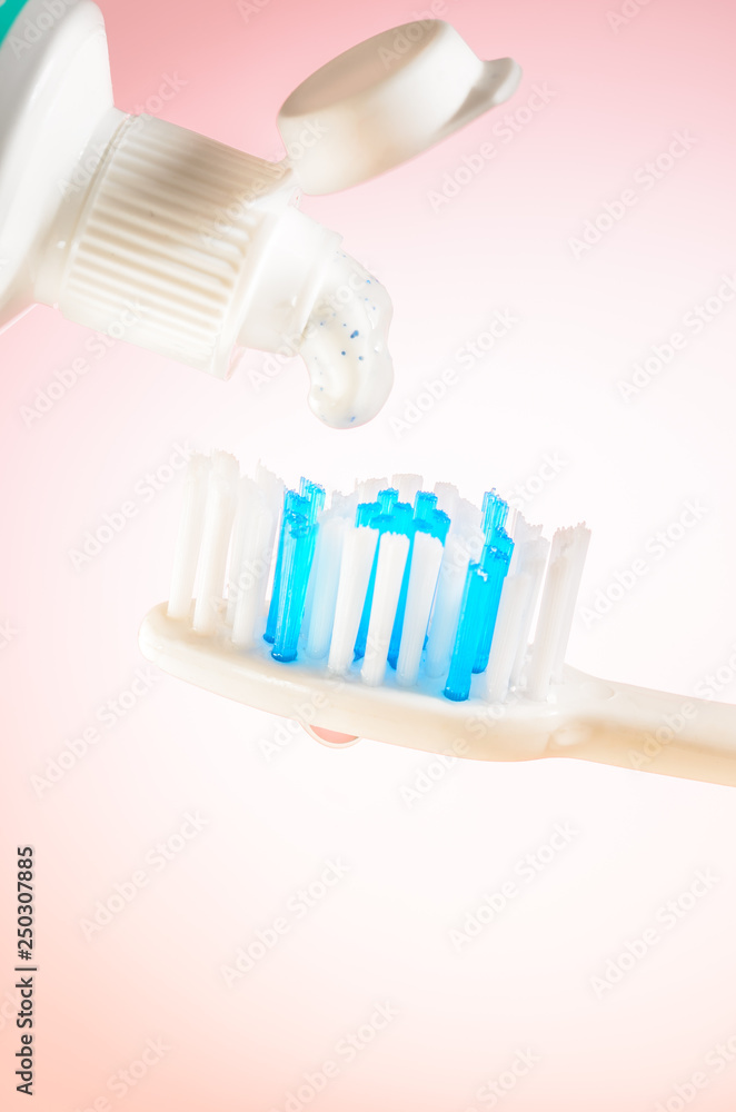 Toothpaste squeezed from tube onto brush on a pink background, close up Toothpaste squeezed from tube onto brush on a pink background, close up