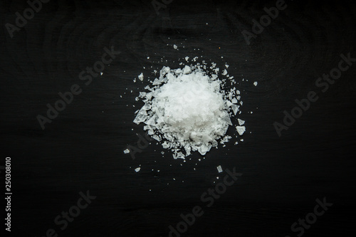 Close-up image of sea salt flakes on black wood background, view above