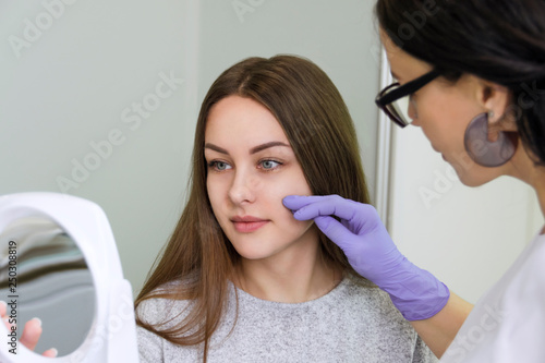 Female cosmetologist showing to young pretty woman the face zones to apply clinic treatment. Medicine, aesthetic and beauty concept