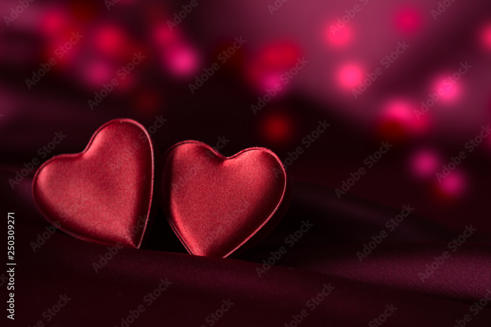 Obraz premium Two red hearts on purple satin with delicate red and purple bokeh in background