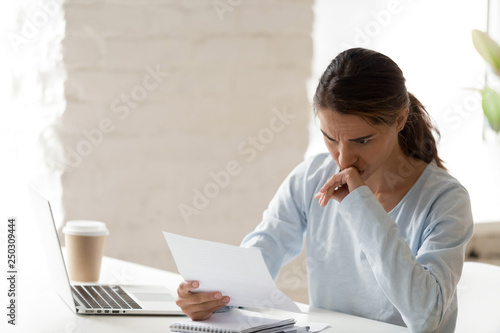 Frustrated young woman sitting at table reading letter photo