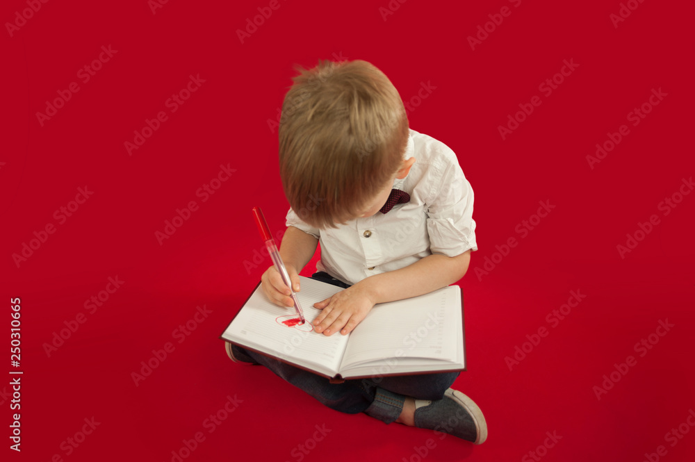 child boy draws in the album on a sheet of red heart on a red background. Concept of family and love child boy draws in the album on a sheet of red heart on a red background. Concept of family and love