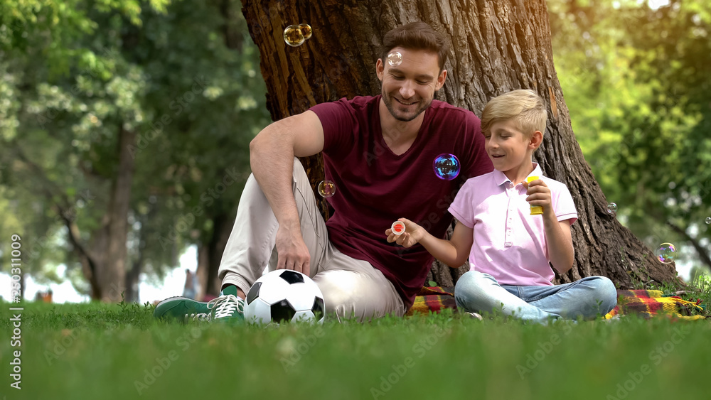 Father and boy enjoying making bubbles in park, family entertainment in weekend Father and boy enjoying making bubbles in park, family entertainment in weekend