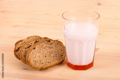 A glass of milk and three pieces of bread on a wooden table