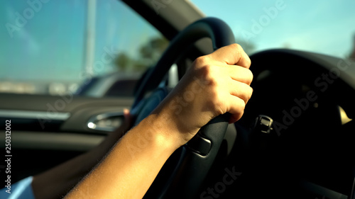 Teenagers hands holding black steering wheel, girl driving car uncertainly