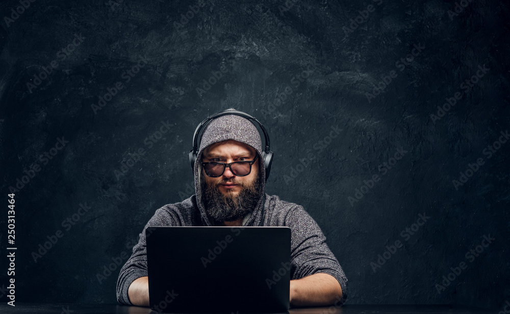 A hacker sits behind a laptop in a dark room and stares intently at the camera A hacker sits behind a laptop in a dark room and stares intently at the camera