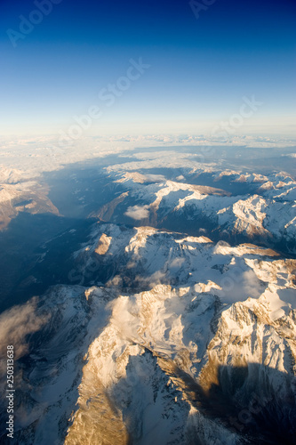 Snowy alpine mountain peaks rise above the cloud layer. Aerial view in the winter.