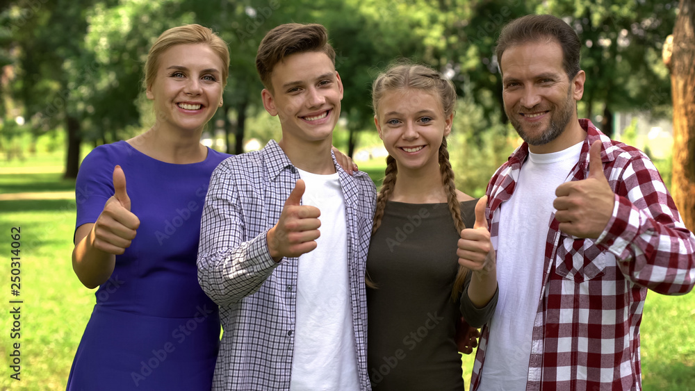Obraz premium Joyful family members enjoying weekend in park and showing thumbs up into camera