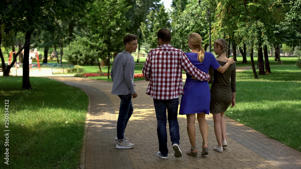 Pleased family members walking in park, enjoying perfect weekend together