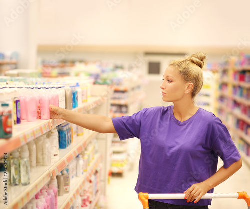 Woman shopping in supermarket reading product information.(washing powder,detergent)