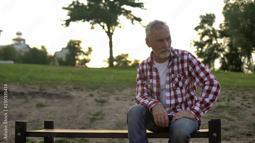 Melancholic elderly male sitting on bench in park and thinking about problems Melancholic elderly male sitting on bench in park and thinking about problems