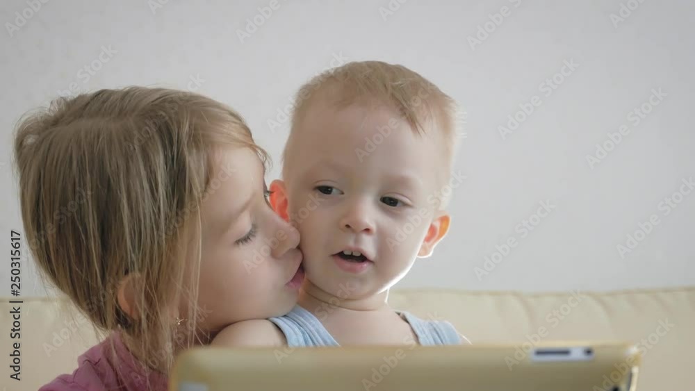 Adorable little brother and sister using digital tablet, smiling and looking happy. Brother and sister having fun at home. Adorable little brother and sister using digital tablet, smiling and looking happy. Brother and sister having fun at home.