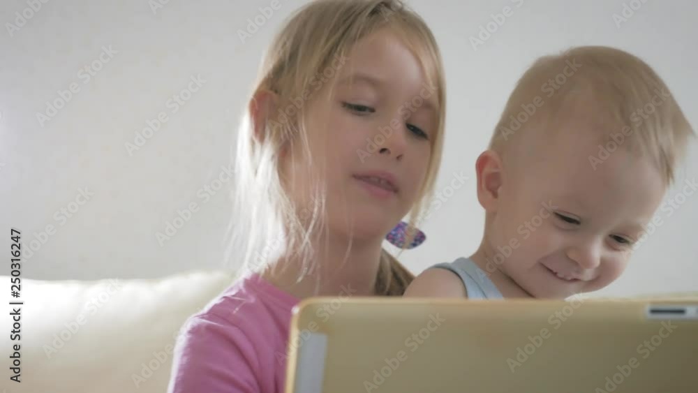 Adorable little brother and sister using digital tablet, smiling and looking happy. Brother and sister having fun at home. Adorable little brother and sister using digital tablet, smiling and looking happy. Brother and sister having fun at home.