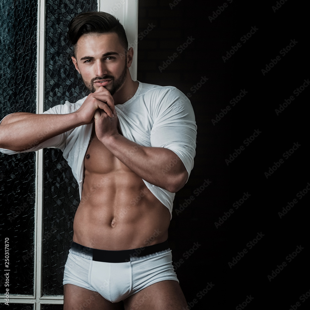 Strong athletic sexy muscular male model wearing white sweater on black  background. Seductive bearded brunette guy in white underwear shows his  perfect six pack abs. Sport and healthy lifestyle. Stock Photo