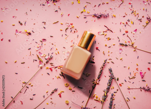golden nail polish and lavender petals on pink background