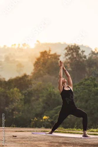 Fototapeta na wymiar Portrait of young female practicing yoga in warrior posture. with the nature during sunrise in the morning. Peaceful, mindfulness and Healthcare concept.
