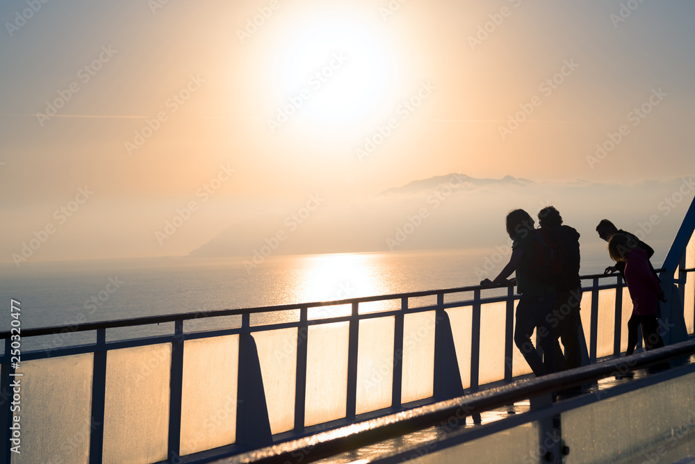 Silhouette of travelers on board watching coastline in mist at sunrise