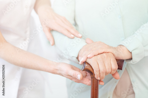 Closeup of senior lady's hands on wooden walking stick, helpful nurse supporting her