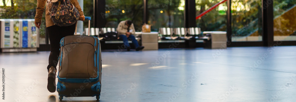 Obraz premium Young woman sitting in the terminal waiting room and waiting for departure, she is texting and connecting with her smartphone