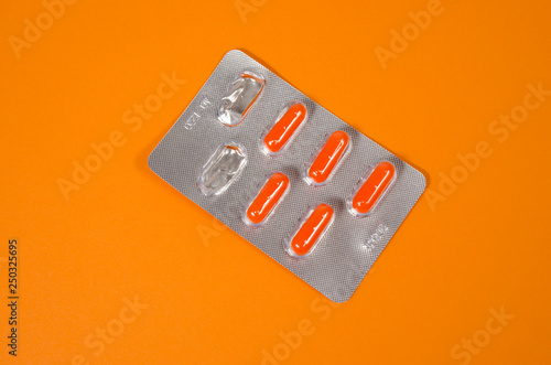 Bright orange tablets in silver packaging on an orange background