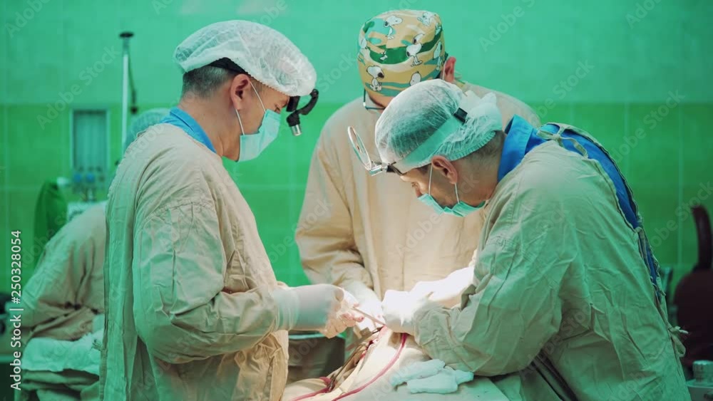 Three surgeons is performing complex surgery on the face of a person in the operating room. A nurse is helping surgeons with tools and materials. Three surgeons is performing complex surgery on the face of a person in the operating room. A nurse is helping surgeons with tools and materials.