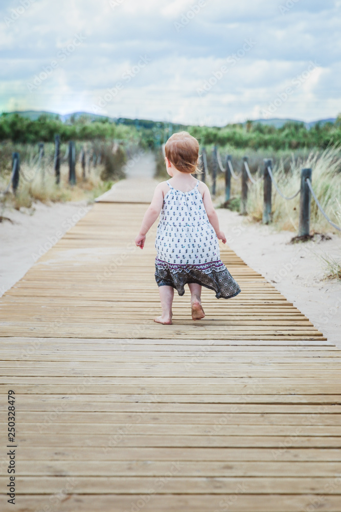 little girl running along a wooden walkway on the beach in summer