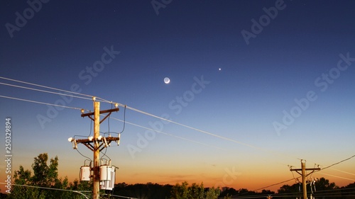 Power lines and moon at sunset.