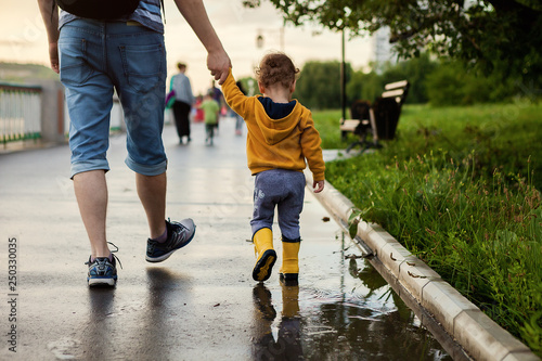 Father and son walking in the fresh air in rubber boots on the puddles after the rain