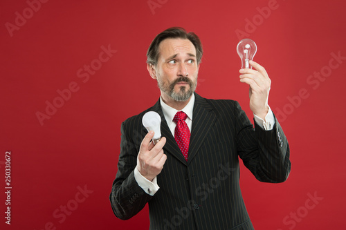 Lighting choices to save money. Man bearded consultant formal suit hold light bulb on red background. Symbol of idea progress and innovation. Environment friendly lighting. Energy efficient lighting